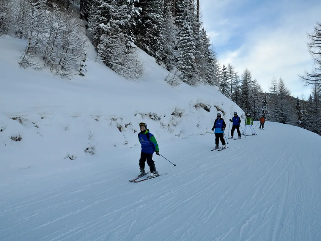 Skifahrer auf der Piste unterhalb der verschneiten Bäume.